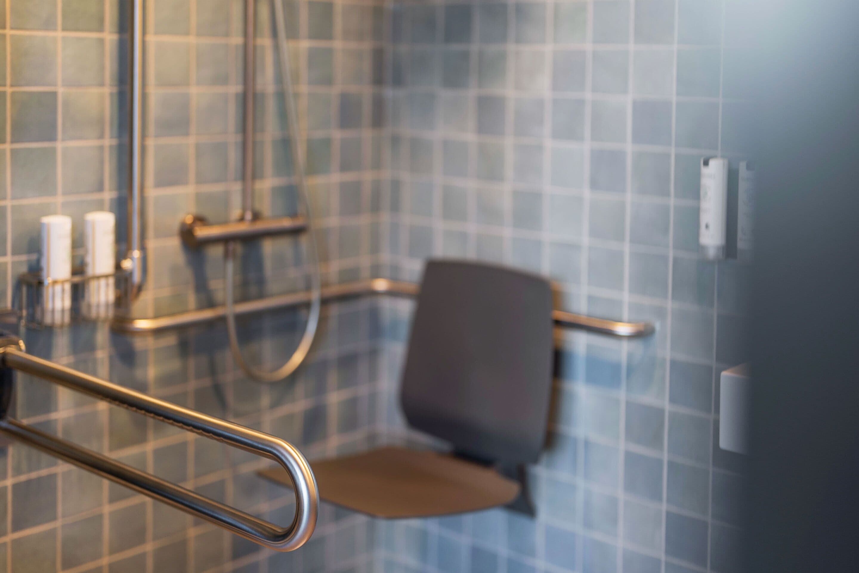Un baño con pared de azulejos azules, asiento de ducha y barra de apoyo.
