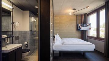 A modern hotel room with a large bed, a bathroom with a shower, and a TV mounted on the wall.