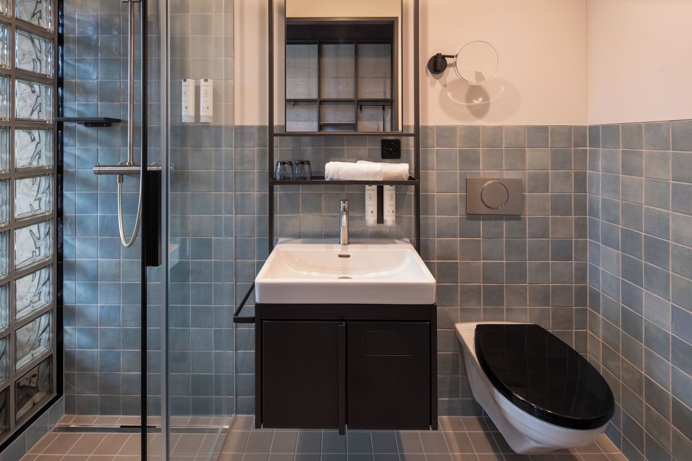 Ein Badezimmer mit Duschkabine aus Glas, einem weißen Waschbecken und einer schwarzen Toilette.