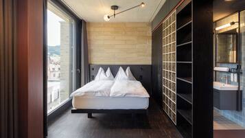 Een moderne hotelkamer met een groot bed, een inbouwkast, een badkamer met spiegel en wastafel, en uitzicht op de stad door het raam.