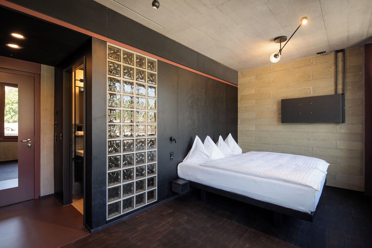 A modern bedroom with a large bed, a sliding glass door leading to a balcony, and a mounted TV on the wall.