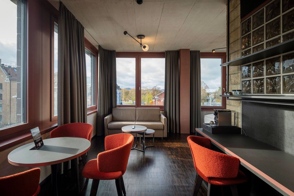 A modern room with a sofa, two red chairs, a small table, and a bar area with a shelf.