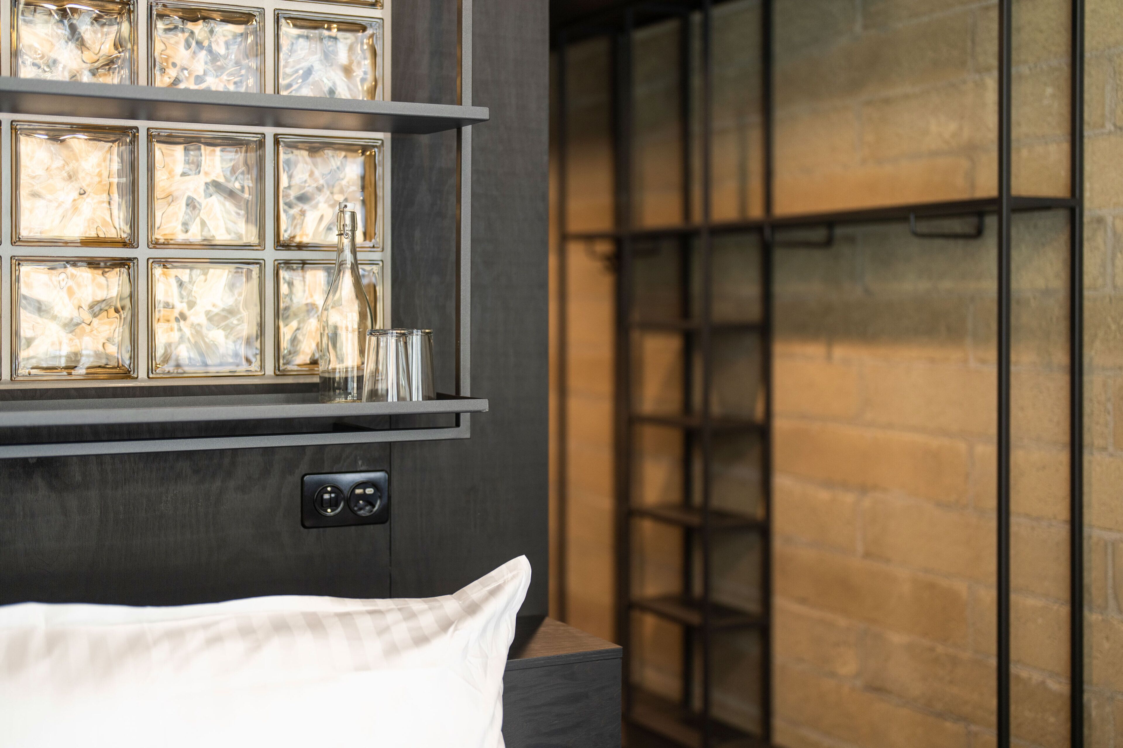 Una habitación moderna con una cama, un estante con paneles de vidrio decorativos y una pared de ladrillo.