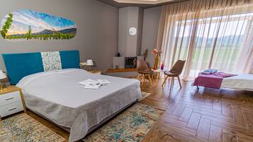 Habitación de hotel con una cama grande, un escritorio con computadora, una silla, una mesita con un florero y una ventana con cortinas.