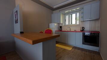Una cocina compacta con una isla de madera, armarios blancos, horno empotrado y una ventana con persianas.