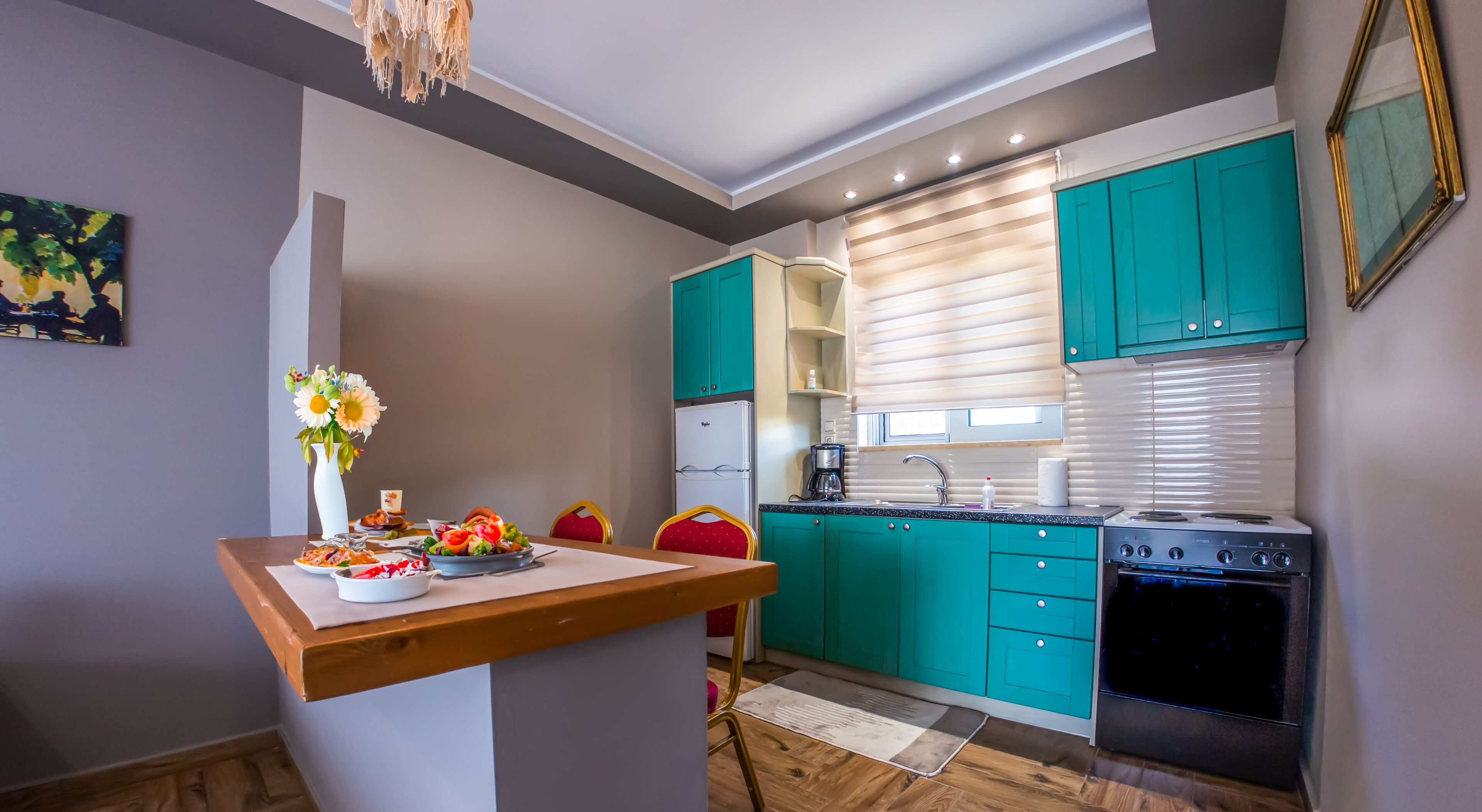 Una cocina compacta con armarios color turquesa, horno empotrado y comedor con mesa y sillas de madera.