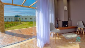 Ein modernes Wohnzimmer mit großem Fenster, Kamin und Blick auf ein Gebäude und einen Weinberg.