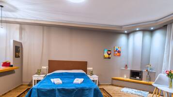Habitación de hotel con cama, mesitas de noche, escritorio, una silla, una pequeña mesa con un florero y obras de arte en las paredes.