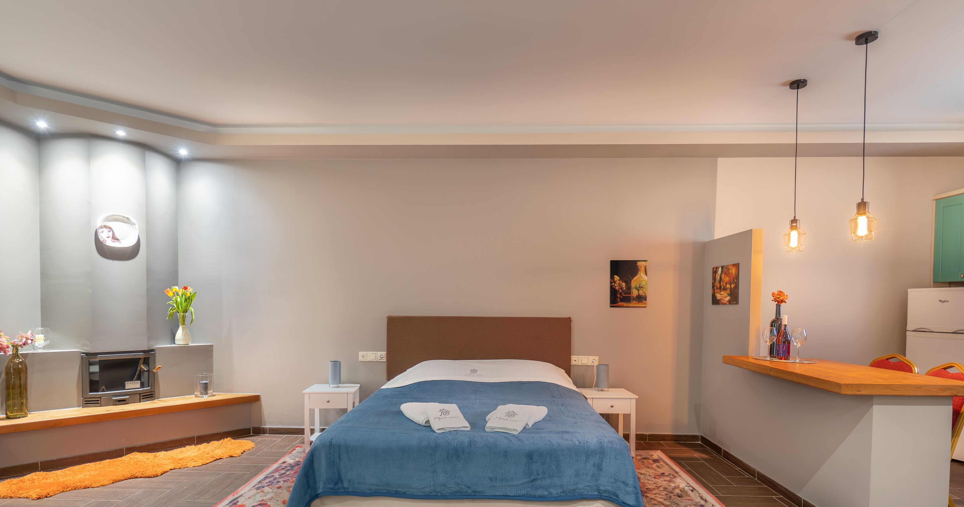 Una habitación de hotel moderna con una cama grande, mesitas de noche, un escritorio pequeño, un espejo y una kitchenette.