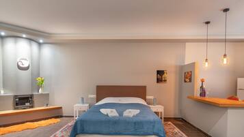 Una habitación de hotel moderna con una cama grande, mesitas de noche, un escritorio pequeño, un espejo y una kitchenette.
