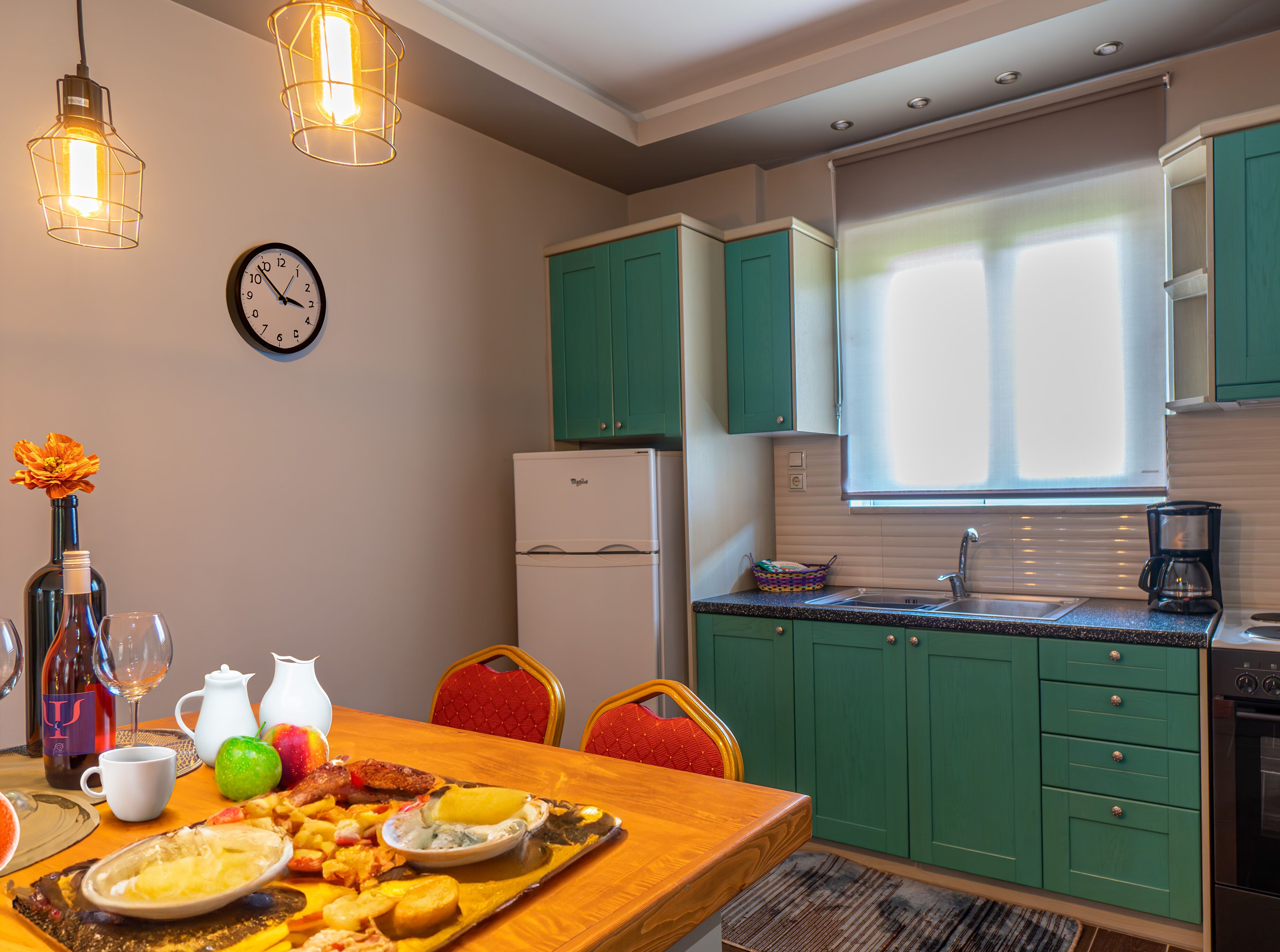 A modern kitchen with teal cabinets, a stainless steel refrigerator, and a dining area with a wooden table set for a meal.