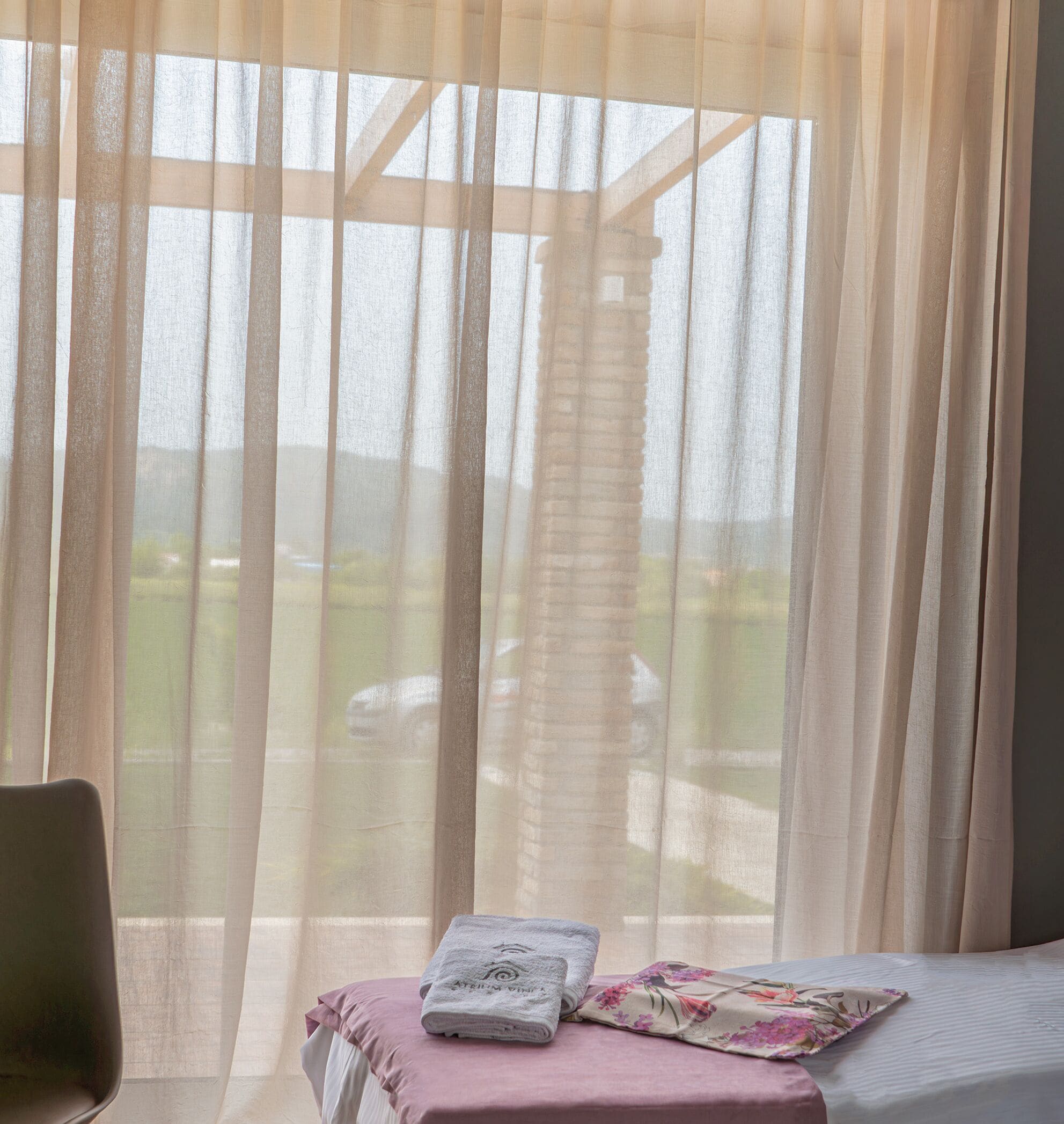 Una habitación con cama, una silla y una ventana con cortinas translúcidas.