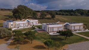 Ein modernes Gebäude mit Solaranlage, einer überdachten Außenbereits und einem Weinberg im Hintergrund.