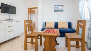 Una sala de estar con un sofá, dos sillas de madera, una mesa de centro, un televisor y un cuadro en la pared.