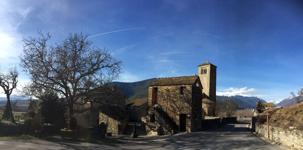 A stone building with a bell tower, surrounded by trees and mountains.