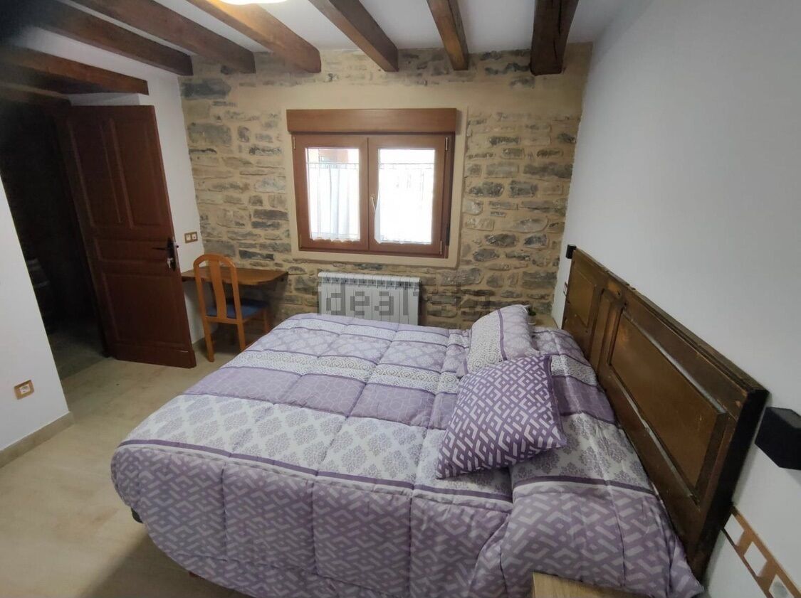 Een slaapkamer met een bed, een houten hoofdbord, een stenen muur, een raam en een radiator.