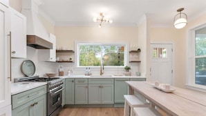 A modern kitchen with light green cabinets, a central island, and a large window providing natural light. - Seagrove Cottage- 4 Bikes Free! (Santa Rosa Beach)