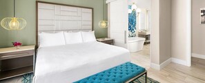 Relax in a serene space with a large bed, nightstand, and bathroom featuring a bathtub and mirror.