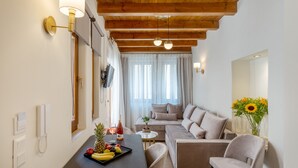 A modern living room with a wooden ceiling, a sofa, a dining table with fruit, and a vase of sunflowers. - Casa Del Balsamo (Rethymno)