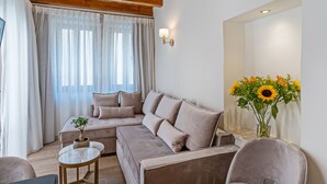 A modern living room with a sectional sofa, a small round table, and a vase of sunflowers. - Casa Del Balsamo (Rethymno)