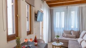 A modern living room with a wooden ceiling, a sofa, a small round table, and a dining table with fruit and wine. - Casa Del Balsamo (Rethymno)