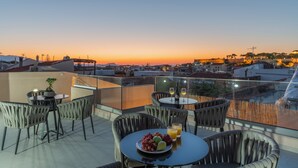 A rooftop terrace with round tables and chairs, a potted plant, and a table with fruit and drinks. - Casa Del Balsamo (Rethymno)