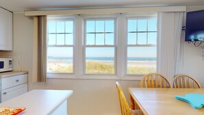 Ein Zimmer mit Küchenzeile, einem Esstisch mit Stühlen und einem großen Fenster mit Blick auf den Strand.