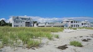 Un hôtel en bord de mer composé de plusieurs bâtiments, dont une grande maison et des constructions plus petites, avec une plage de sable en premier plan.