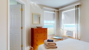 A bedroom with a bed, a wooden dresser, a chair, and a window with a view of the beach.