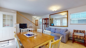 A spacious living room with a wooden dining table, striped sofa, and a large mirror.