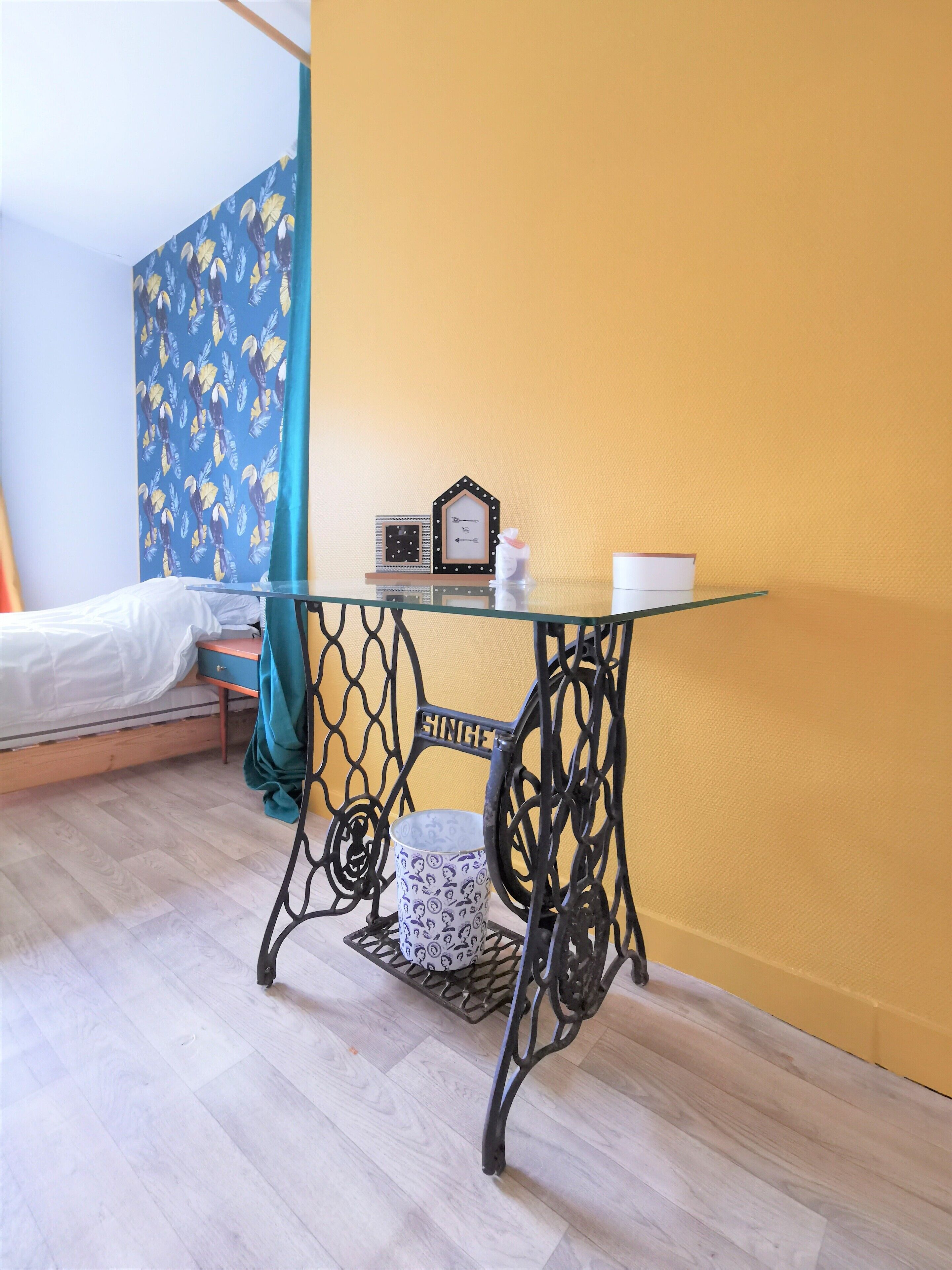 A room with a bed, a table with a glass top, a clock, and a curtain.