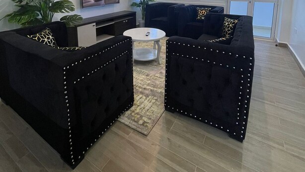 A modern living room with a black sofa set, a TV, and a ceiling fan. - Santorina Home Suites (Kisii)