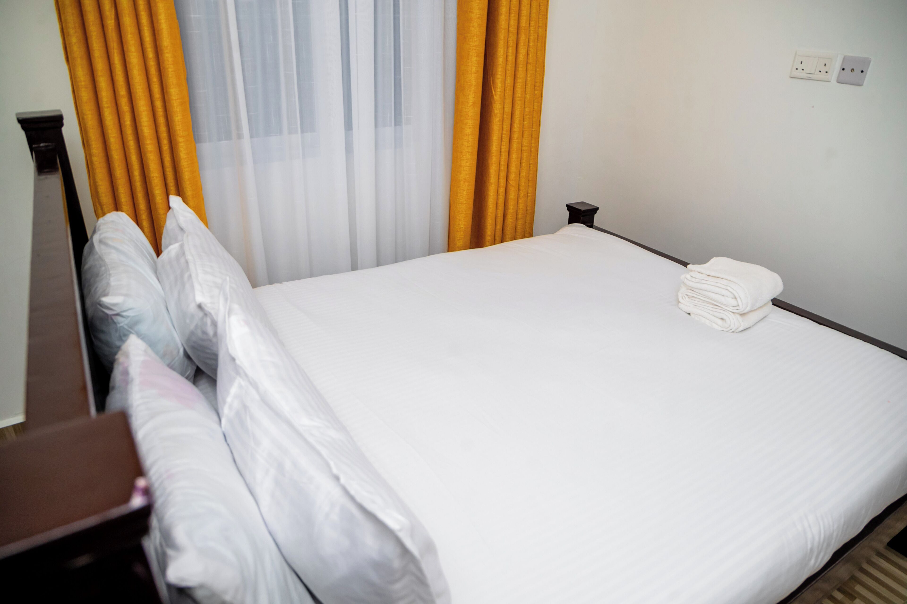 Een netjes opgemaakt bed met witte lakens en een opgevouwen handdoek ernaast.