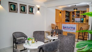 A hotel lobby with grey upholstered chairs, a white round table, and a bar area with wooden paneling. - Santorina Home Suites (Kisii)