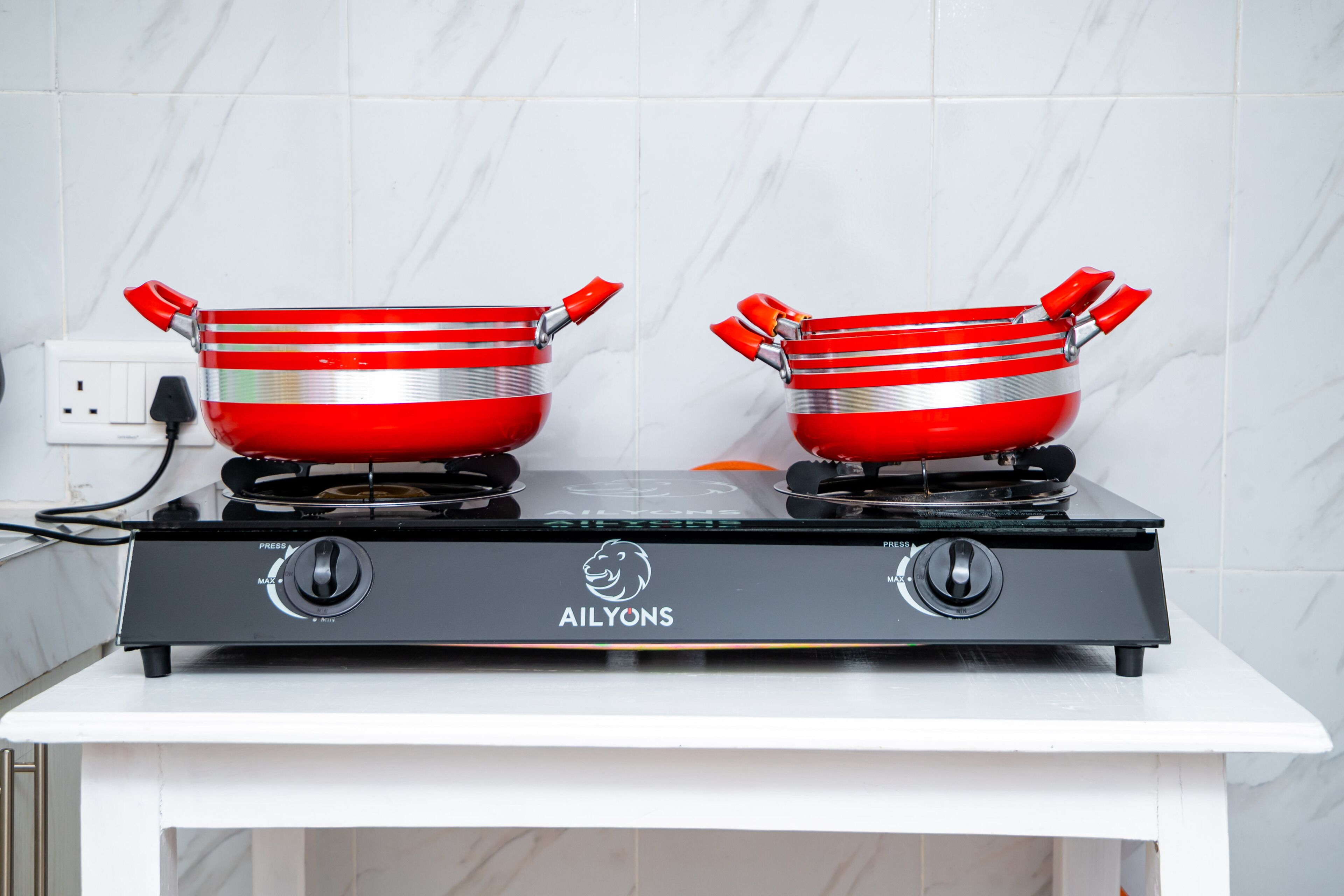 Une cuisine équipée d’une cuisinière à gaz et de deux casseroles rouges posées sur les brûleurs.