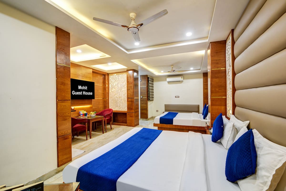 A hotel room with two beds, a desk, a chair, and a TV screen displaying "Mohit Guest House".