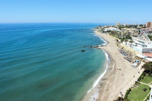 An aerial view of a coastal area with a beach, buildings, and a clear sky. - Homely 3 bedroom apt in Riviera close to beach (Mijas Costa)