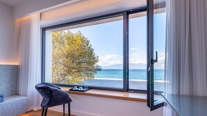 A modern room with a large window overlooking a body of water and a tree. - Amario Suites Hotel (Aigialeia)