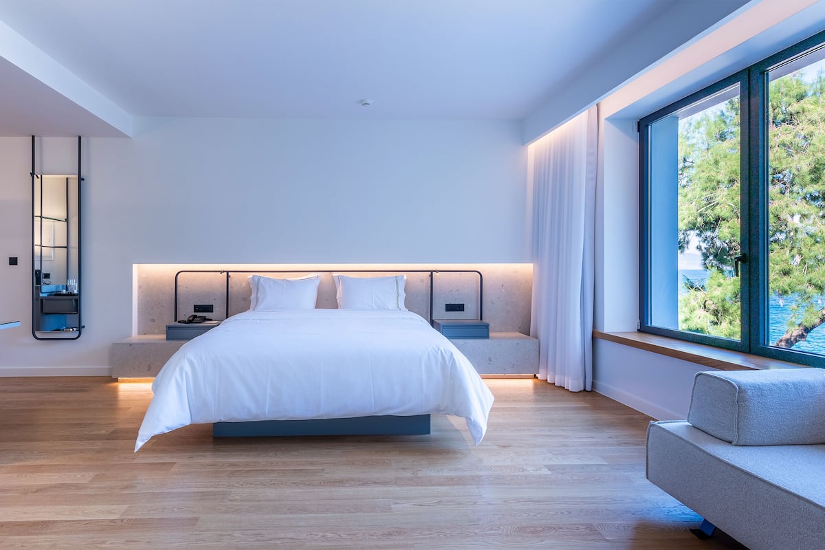 Un dormitorio moderno con una cama grande, mesitas de noche, un sofá y vistas al exterior.