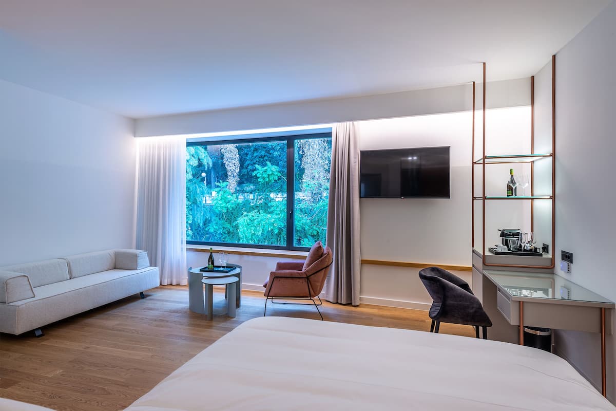 Una habitación de hotel moderna con un ventanal grande, una cama, un escritorio, una silla y un televisor.