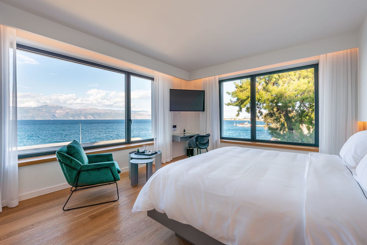 Una habitación de hotel moderna con una cama grande, un escritorio y una silla, todo con vistas panorámicas al mar y las montañas.