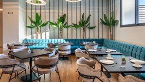 A modern dining area with a teal sofa, round tables, and chairs. - Amario Suites Hotel (Aigialeia)