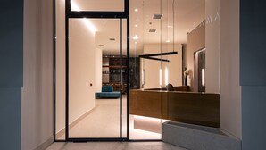 A modern interior with a glass entrance, a reception desk, and a bar area visible through the glass doors. - Amario Suites Hotel (Aigialeia)