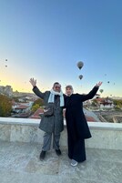 Dos personas en la azotea alzan los brazos, contemplando una vista de la ciudad con edificios y globos aerostáticos en el cielo.