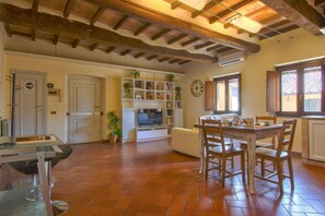 Un salón amplio con suelo de baldosas, una mesa de comedor con sillas, un sofá, una estantería y un reloj en la pared.