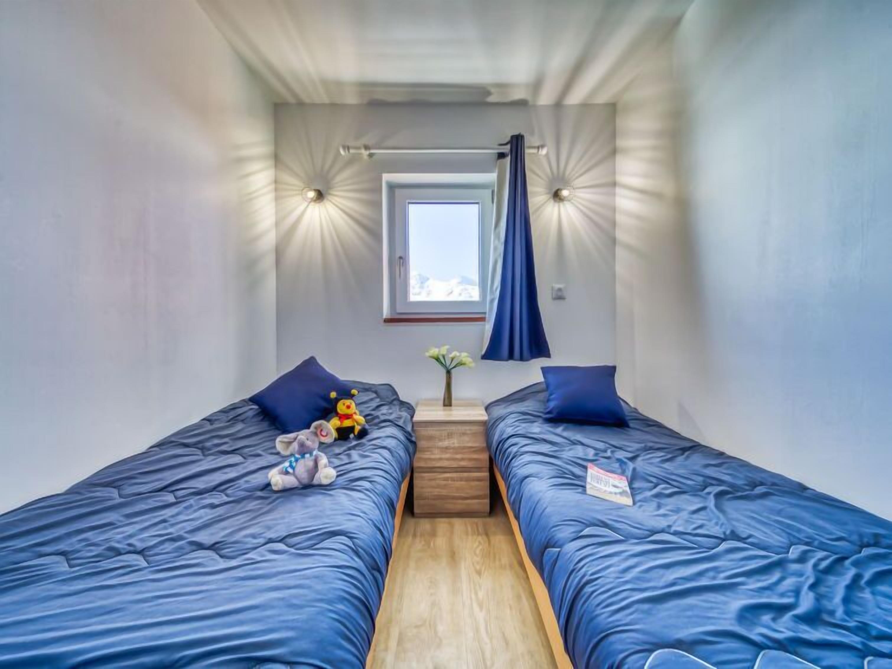 Een kleine kamer met twee eenpersoonsbedden, een klein raam en een plafondlamp.