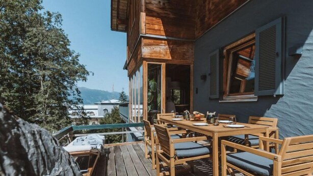 Terraza de madera con una mesa y sillas, con vista a un paisaje montañoso.
