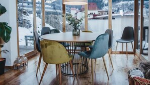 Un interior de madera con una mesa redonda y sillas, ventanas amplias con vistas a un paisaje nevado y una lámpara colgante.