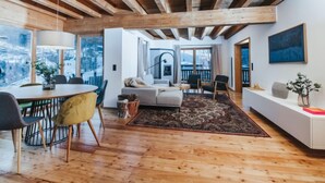 Amplia sala de estar con techo de madera, una mesa de comedor con sillas, un sofá y un gran ventanal con vistas a las montañas.
