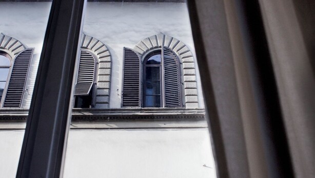 Une vue d’un bâtiment aux fenêtres en arc de cercle et à la façade en briques, prise à travers une fenêtre à cadre noir.